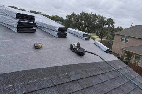Bundles of architectural shingles on a roof slope beside a nail gun and chalk line