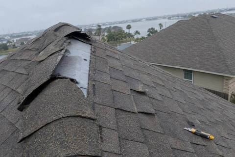 Ridge cap shingles lifted and torn along the peak of a two-story roof after a wind event