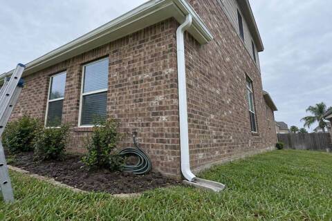 White seamless gutter and downspout on the corner of a brick two-story house